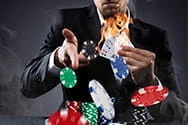 Ein Casino Dealer hält brennende Karten in der Hand. Davor fliegen Chips durch die Luft.