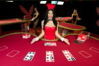 Ein Dealer in einem roten Playboy Bunny Kostüm sitzt hinter einem Live Blackjack Spieltisch der Firma Microgaming. Links dahinter ist eine weitere Frau im Bunny Kostüm zu erkennen, die neben einem großen Playboy Logo posiert.