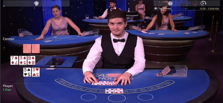 Live Casino Hold'em von Ezugi im Live Casino Bereich von Betchan. Der Spieler hat ein 3er Paar auf der Hand, die Karten des Dealers sind noch nicht aufgedeckt. Im Bildhintergrund sind weitere Spieltische zu erkennen.