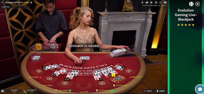 Live Blackjack VIP B von Evolution Gaming im Live Bereich von Casino Room. Der Dealer am Tisch greift gerade nach neuen Karten. Links hinter den Tisch steht ein weiterer Dealer, der zusätzliche Spielkarten mischt.