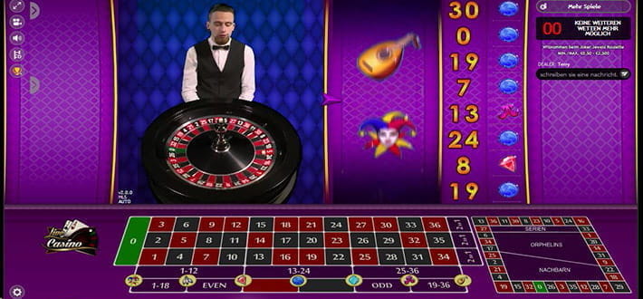 Joker's Jewels Live Roulette von Extreme Live Gaming im Live Casino von DrückGlück. Im Vordergrund befindet sich das Setztableau. Links oben ist in einem kleinen Fenster der Croupier hinter dem Kessel stehend eingeblendet. Den rechten oberen Bildbereich füllen die zusätzlichen Walzen des Spiels aus.