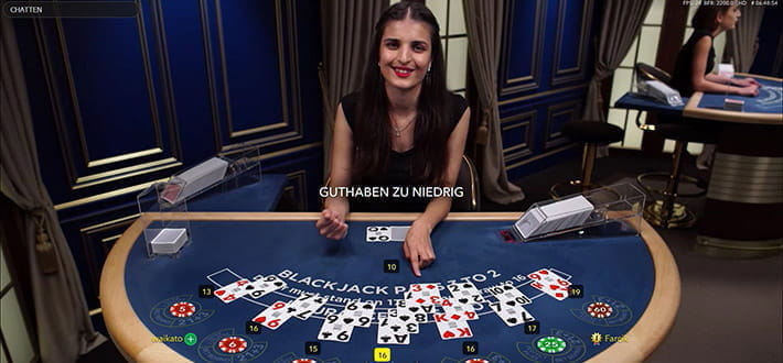 Ein Live Blackjack Classic Spieltisch von Evolution Gaming im Live Casino von Gate 777. Am Tisch sitzen 7 Spieler. Der Dealer zeigt mit seiner linken Hand auf die Karten des Spielers in der Mitte. Im Hintergrund ist rechts ein weiterer Spieltisch zu erkennen.