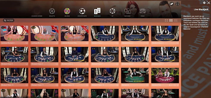 Ein Exclusive Blackjack Tisch im Live Casino. Der Spieltisch wird von Evolution Gaming bereitgestellt. Der Dealer fragt gerade einen der Spieler, ob er eine zusätzliche Karte erhalten möchte. Im Bildhintergrund sind weitere Spieltische zu erkennen.