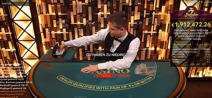 Ein Live Casino Hold'em Spieltisch im Live Casino Bereich des NetBet Casinos, zur Verfügung gestellt von Evolution Gaming. Während links im Bild die Gewinner der letzten Spielrunde durchlaufen, entnimmt der Dealer dem Kartenschlitten die neuen Spielkarten, rechts im Bild ist der aktuelle Stand des Jumbo7 7 Jackpots zu erkennen.