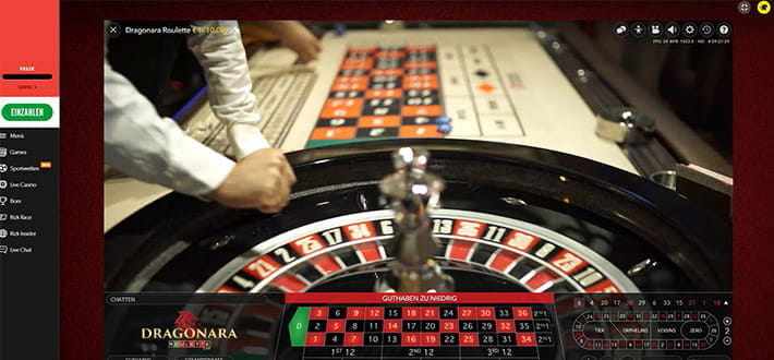 Dragonara Live Roulette von Evolution Gaming im RIZK Live Casino. Im unteren Bildviertel ist das Setztableau. Darüber filmt die Kamera über den Roulettekessel hinweg das Spielgeschehen. Die rechte Hand des Croupiers wirft gerade von links aus die Spielkugel in den Kessel.