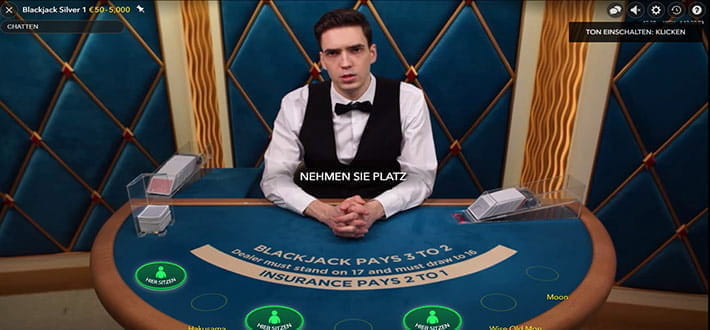 Ein Live Blackjack VIP Spieltisch von Evolution Gaming im VulkanVegas Casino. Alle Spielkarten liegen offen. Der Dealer fragt, einen der Spieler am Tisch, ob er eine weitere Karte erhalten möchte.