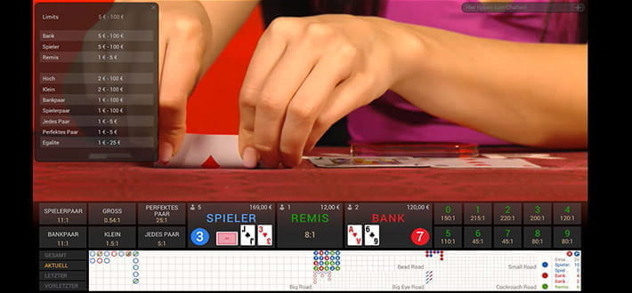 Live Prestige Mini Baccarat des Herstellers Playtech im Winner Live Casino. In Großaufnahme sind die Fingerspitzen des Dealers zu sehen, der das berühmte Squeeze Ritual vor dem eigentlichen Aufdecken der Karte zelebriert.