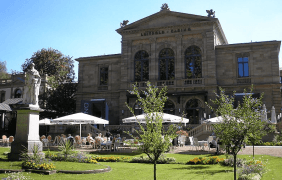 Das Bild zeigt die Aussenansicht des Casinos in Bad Kissingen. Zu sehen ist eine zweistöckige Villa und eine Gartenlage mit einer Statue.