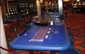 Blick auf den Roulettetisch des Bordcasinos des Kreuzfahrtschiffes Norwegian Dawn&quot, im Hintergrund weitere Spieltische und Spielautomaten.