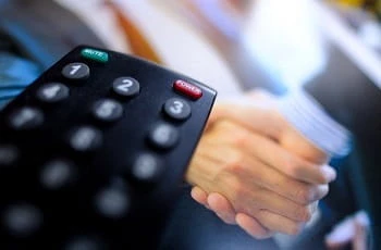 Eine TV-Fernbedienung zeigt auf einen Handshake.