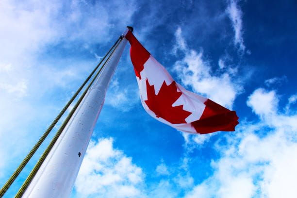 Die kanadische Flagge von unten weht vor blauem, bewölktem Himmel im Wind.