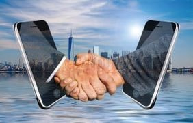 Ein digitaler Handschlag vor eine Städteskyline.