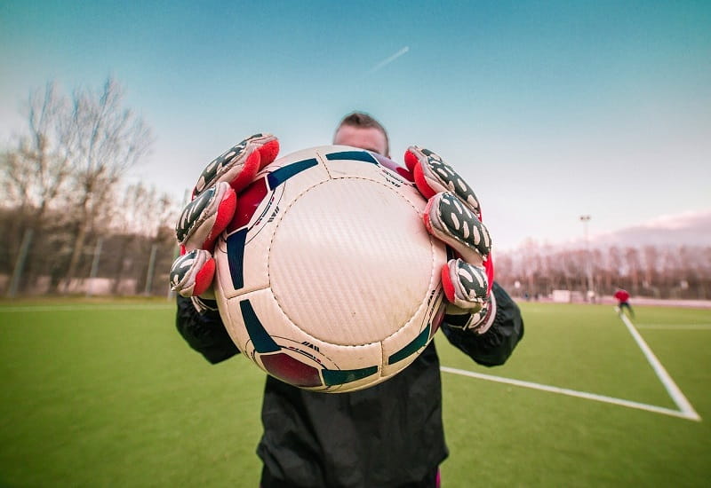 Ein Torwart hält einen Fußball in den Händen.