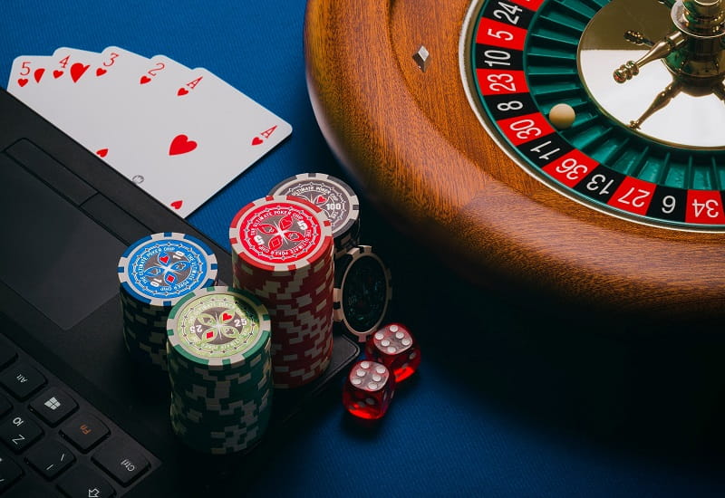 Spielkarten, Würfel, Spielchips und Roulette neben einem Laptop.