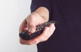 Eine Person hält eine TV-Fernbedienung in der Hand.