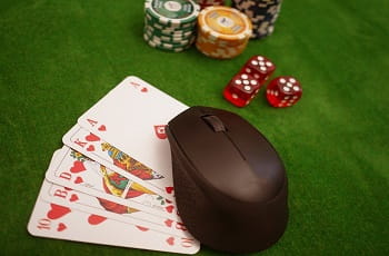 Spielchips, Würfel, Karten und Computermaus auf einer grünen Tischfläche.