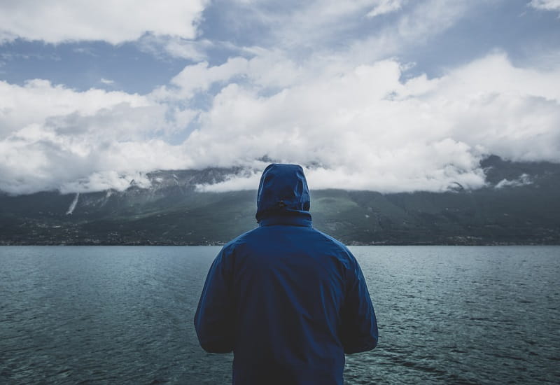 Eine Person mit Kapuze blickt auf den Luganersee.