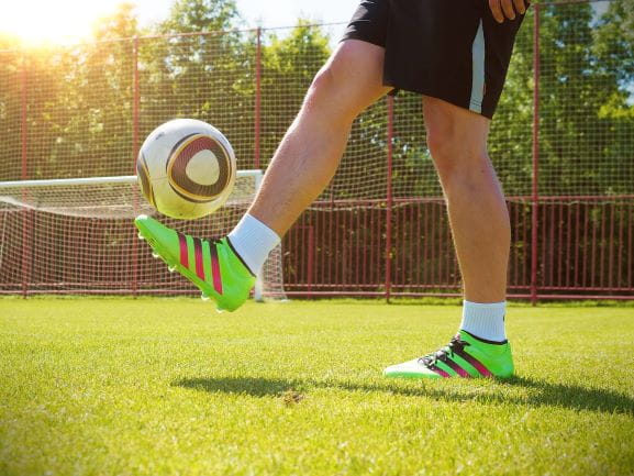 Man hält auf einem Fußballplatz einen Ball hoch.