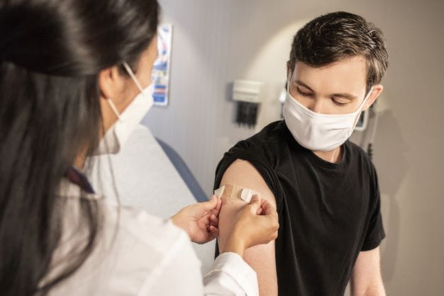 Ärztin klebt Patient ein Pflaster auf die Stelle der Impfung.