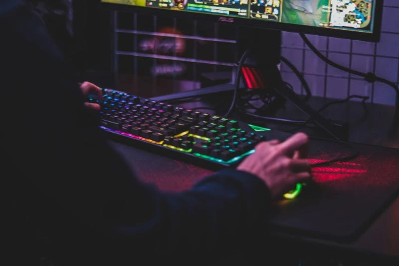 Seorang pria sedang duduk di depan layar PC dan memainkan video game dengan saksama.