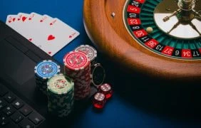 Ein Spieltisch auf dem ein Laptop steht, daneben ein Roulettekessel, Spielkarten und Spielchips.