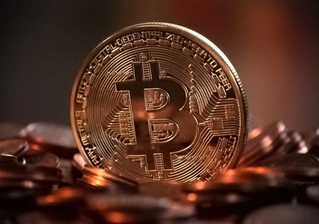 Eine Münze in Bronze mit dem Bitcoin-Zeichen steht auf anderem Kleingeld.