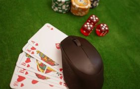 Eine Maus liegt mit Karten, Chips und Würfeln auf einem Pokertisch.