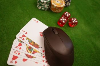Eine Maus liegt mit Karten, Chips und Würfeln auf einem Pokertisch.