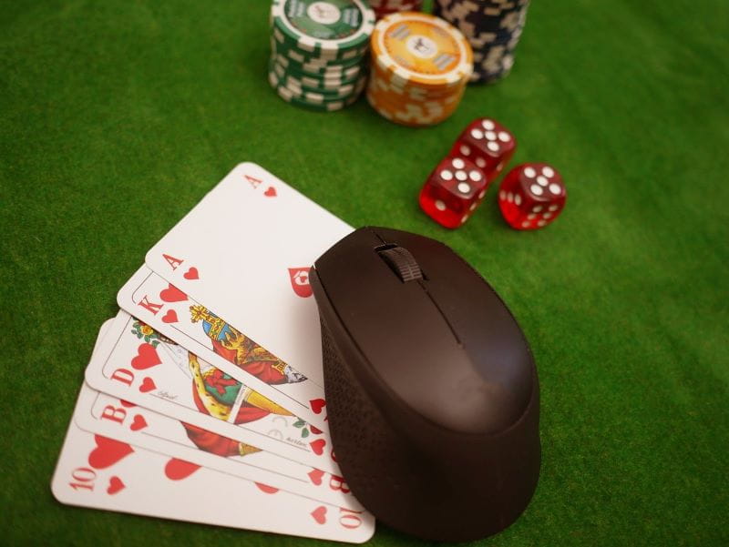 Eine Maus liegt mit Karten, Chips und Würfeln auf einem Pokertisch.