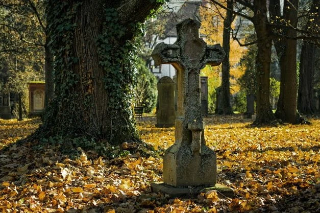 Ein Kreuz steht auf einem Friedhof im Wald.