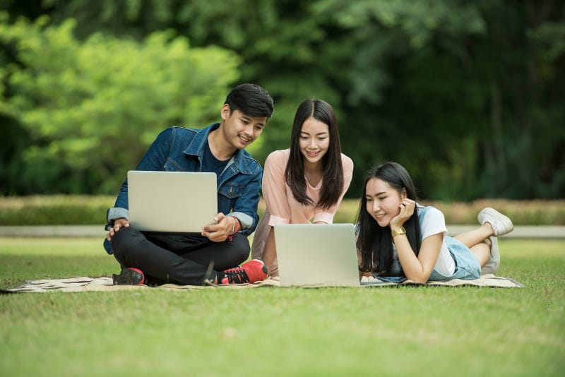 Teman-teman sibuk dengan laptop mereka di taman.