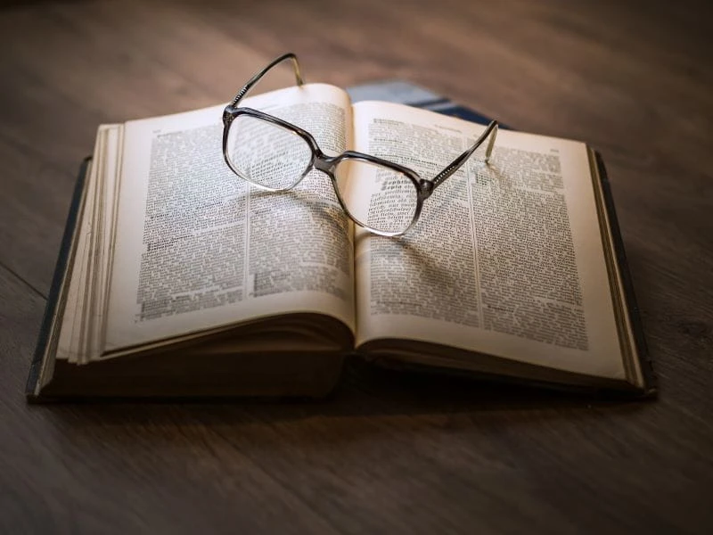 Sepasang kacamata terletak di atas buku yang terbuka.