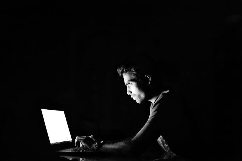 Seseorang sedang duduk di depan laptop dalam kegelapan.