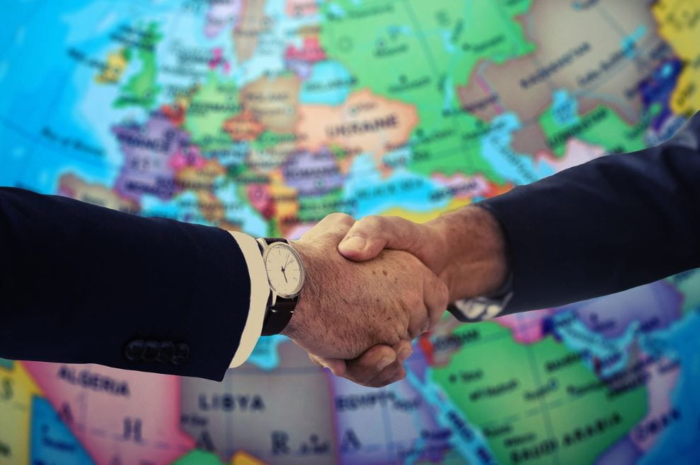 Dua pria berjabat tangan di atas peta Eropa.