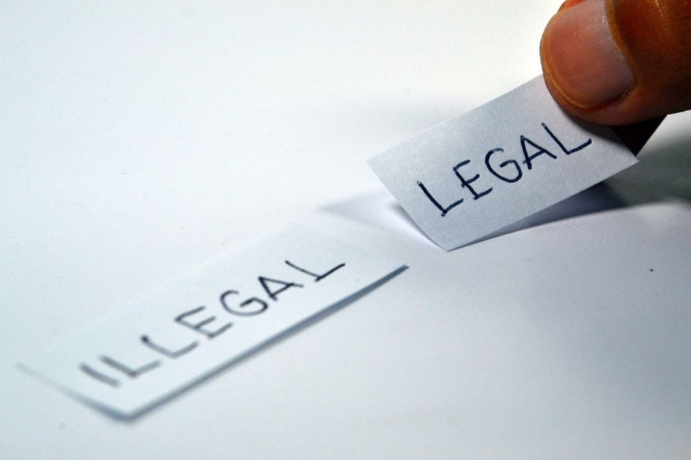 Dua lembar kertas bacaan legal dan ilegal dipegang berdampingan.