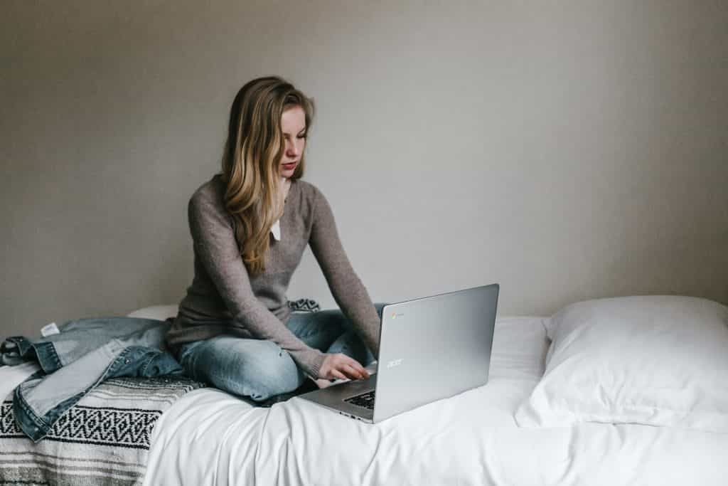 Eine Frau sitzt auf dem Bett und benutzt einen Laptop