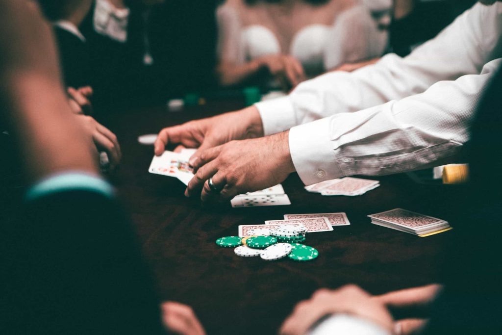 Seorang dealer poker memiliki dua kartu terbuka di tangannya.  Keripik dan kartu lainnya ada di atas meja.