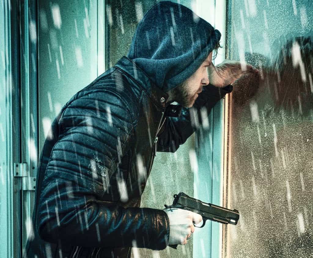 Pria bertudung dengan pistol di dekat pintu kaca