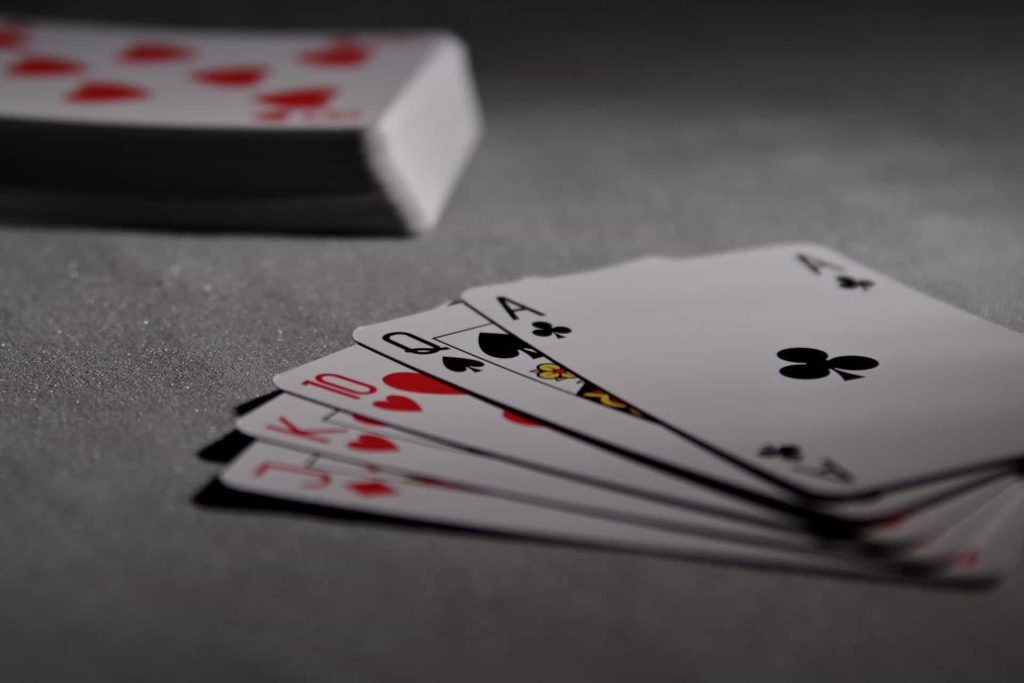 Fünf offene Pokerkarten liegen neben einem Stapel weiterer Karten auf einem Tisch.
