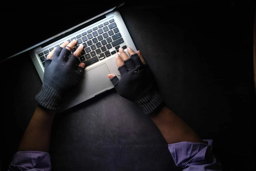 Eine zwielichtige Person mit Handschuhen tippt auf einem Computer