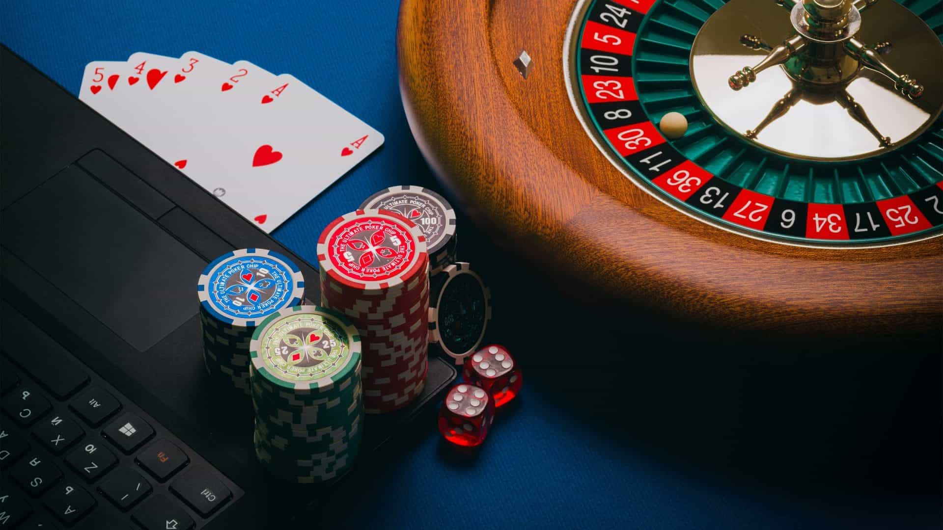 Ein Laptop mit Poker-Chips, Spielkarten und Roulette-Kessel.