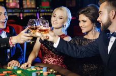 4 Personen sitzen an einem Casino-Tisch und prosten sich mit Getränken zu.