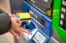 Ein Mensch hält eine Debitkarte in der Hand und führt sie in einen Automaten ein.