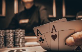 Zwei Asse als Startkarten auf einem Pokertisch, umgeben von bunten Chips, während andere Spieler sich auf ihre Karten konzentrieren.