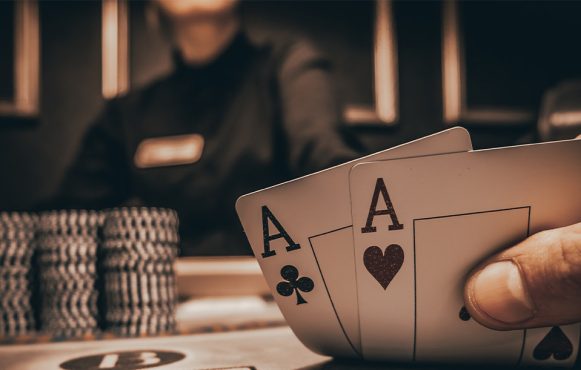 Zwei Asse als Startkarten auf einem Pokertisch, umgeben von bunten Chips, während andere Spieler sich auf ihre Karten konzentrieren.
