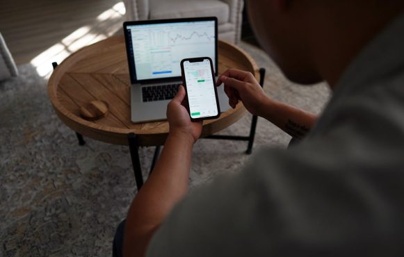 Mann vor Laptop und Smartphone mit Aktienkursen.
