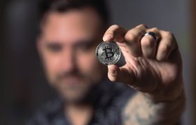 Ein Mann hält eine symbolische Bitcoin-Münze in der Hand