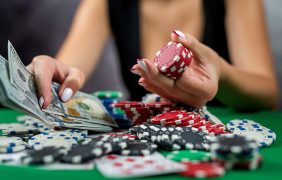 Eine weibliche Person sitzt vor einem Pokertisch mit vielen Pokerchips und Karten und hält eine Menge Geldscheine in der Hand.