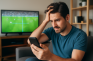 Ein Mann, der traurig auf sein Smartphone schaut und sich die Haare nach einer verlorenen Wette rauft.