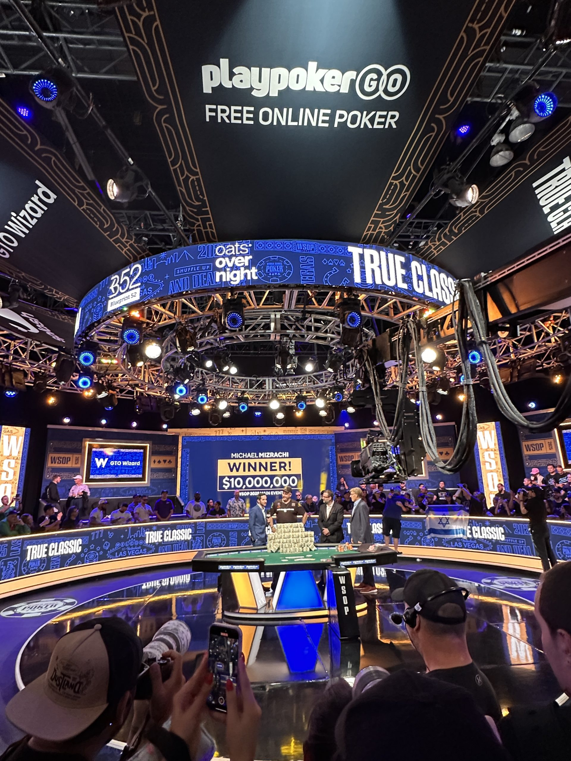 Ein Pokertisch im Finale der WSOP 2025 auf einer Bühne mit den Moderatoren und dem Gewinner Michael Mizrachi.